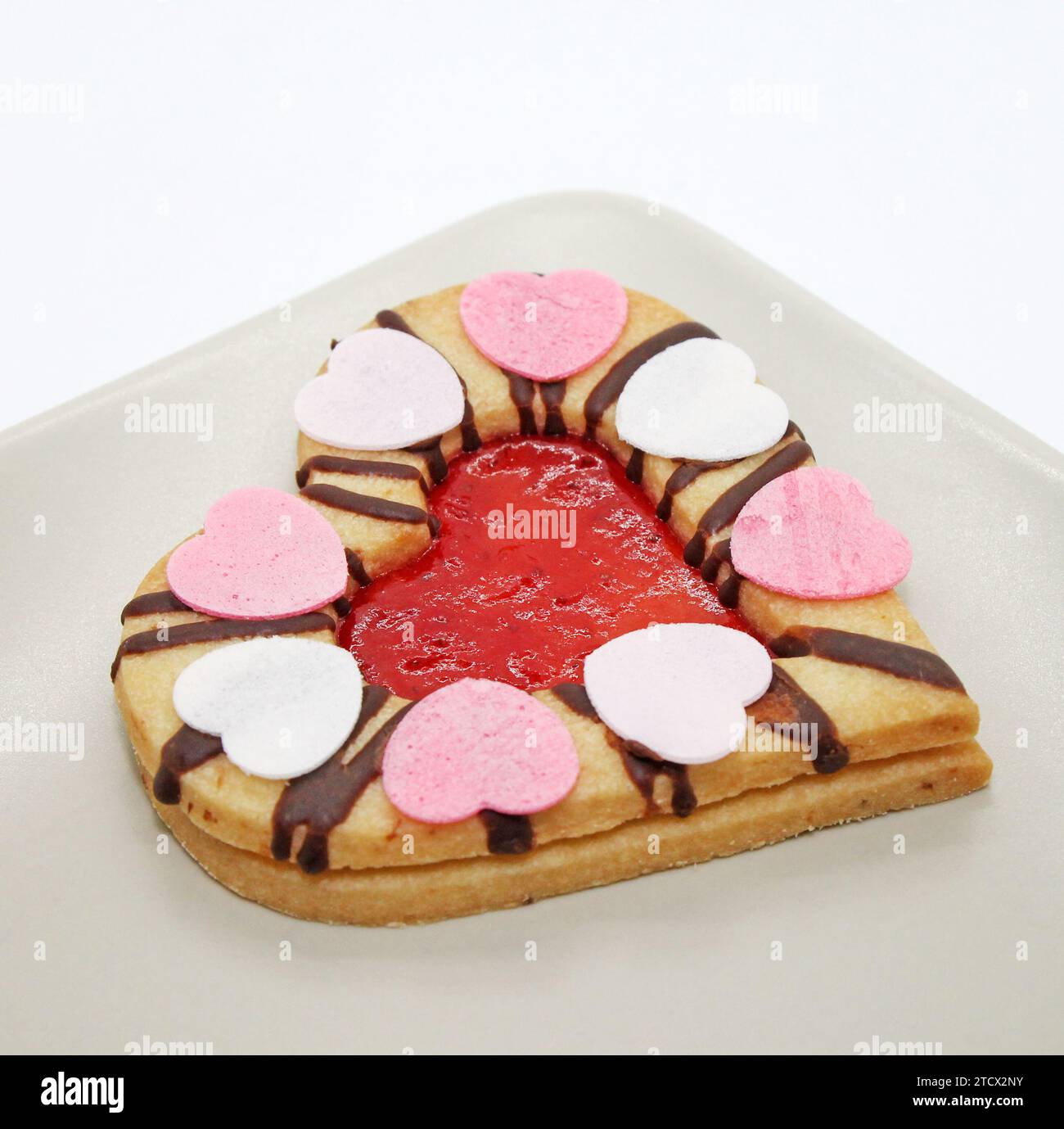 Herzförmiger Keks mit Erdbeermarmelade isoliert auf weißem Hintergrund. Traditionelle Linzer Kekse auf dem Teller Nahaufnahme. Stockfoto
