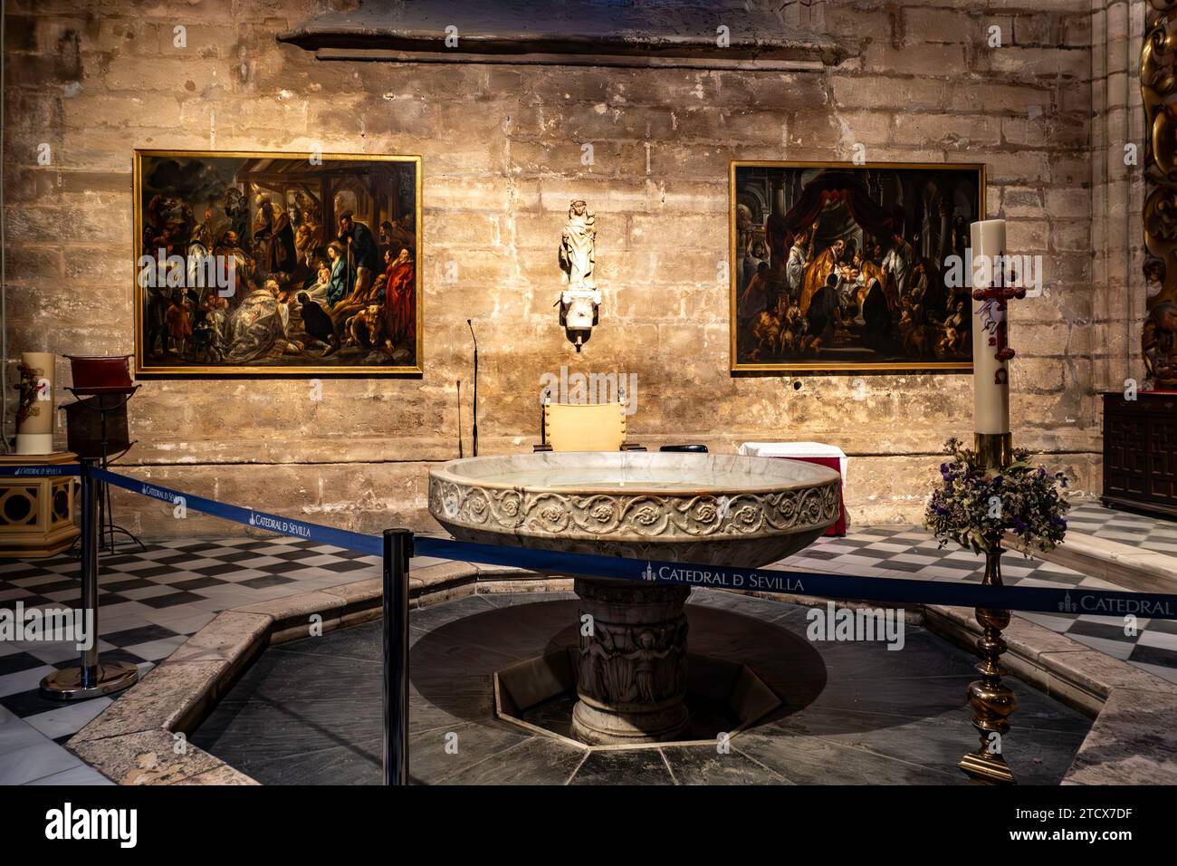 Eine ruhige Taufkammer in der Kathedrale von Sevilla mit einem Marmorbecken, religiösen Gemälden und einer eleganten Kerze, die die heilige Atmosphäre einfangen. Stockfoto