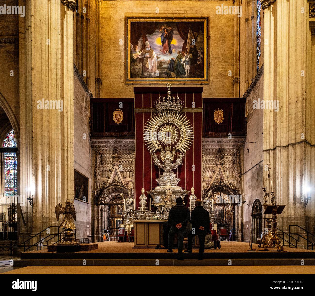 Zwei Personen in Besinnung vor dem reich verzierten Altaraufsatz und dem großen Gemälde in der majestätischen Umgebung der Kathedrale von Sevilla. Stockfoto