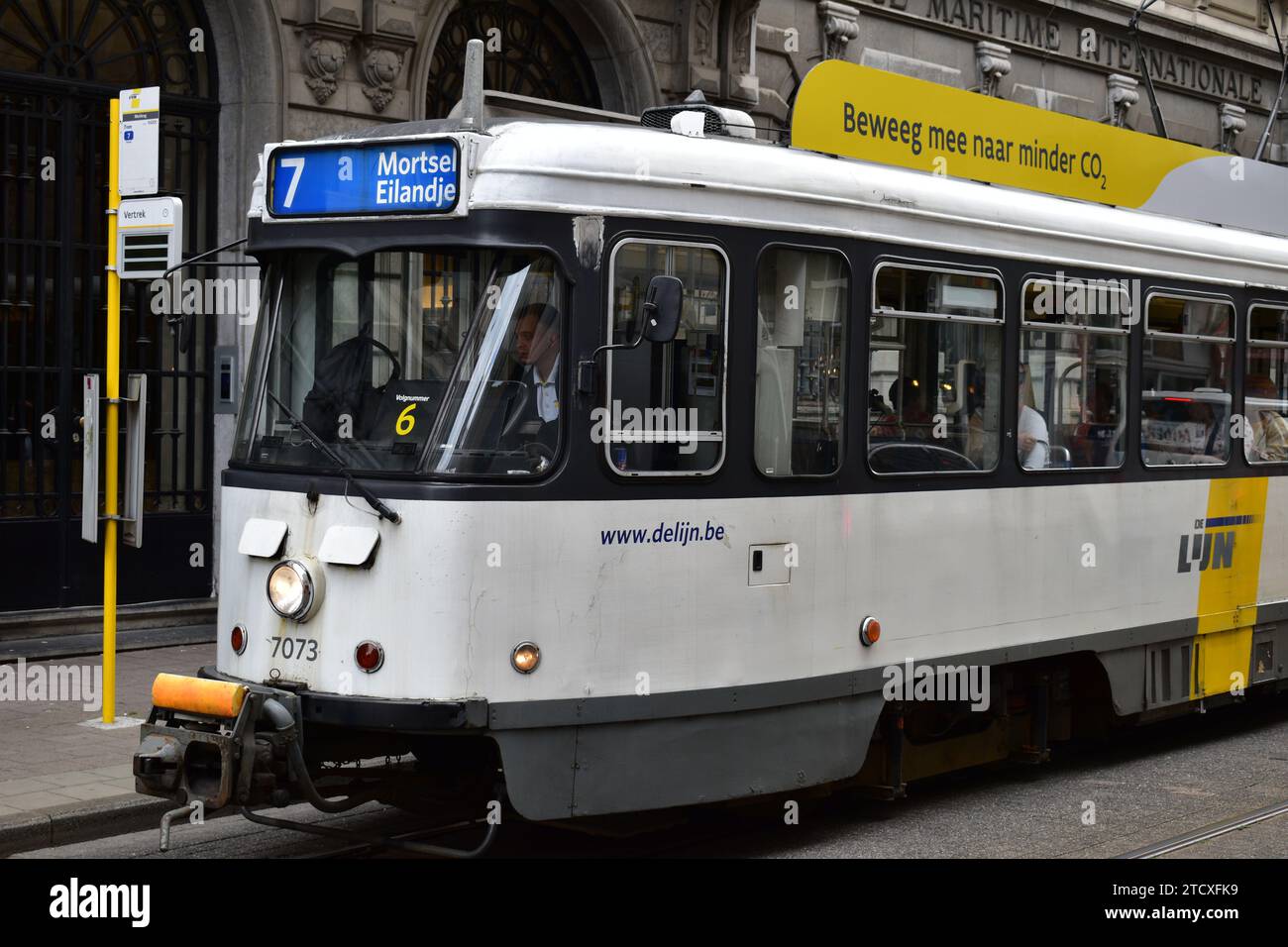 Weiß-gelbe Straßenbahn Nr. 7 in Antwerpen mit Endstation „Mortsel Eilandje“ und Banner-Text oben auf Niederländisch „Move along towards less CO2“ Stockfoto