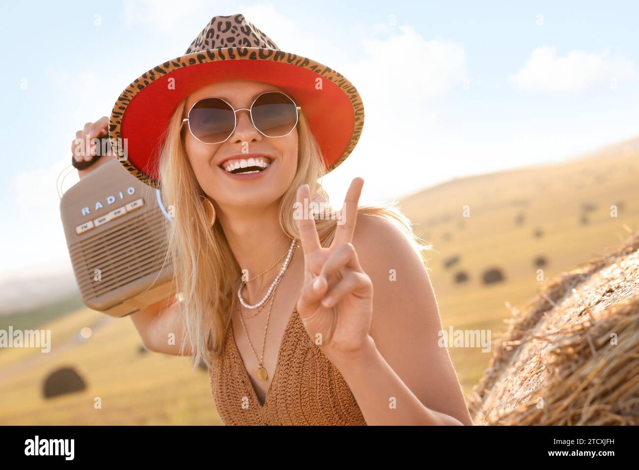 Glückliche Hippie-Frau mit Funkempfänger, die Friedenszeichen im Feld zeigt Stockfoto