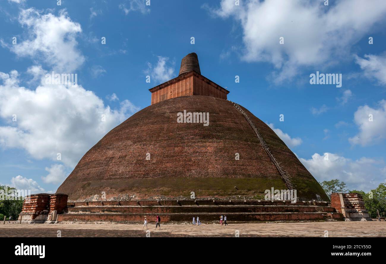 Touristen spazieren um den Fuß des roten Backsteins Jetavanaramaya (Jetavaranama) Dagoba an der antiken Stätte von Anuradhapura in Sri Lanka. Stockfoto