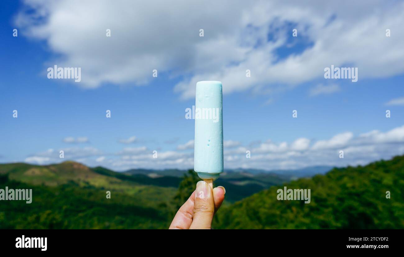 Schließen Sie eine Hand, die einen Eisstock hält, mit einem unscharfen Hintergrund einer Landschaftsansicht auf Berg, Himmel und Wolken Hintergrund. Stockfoto