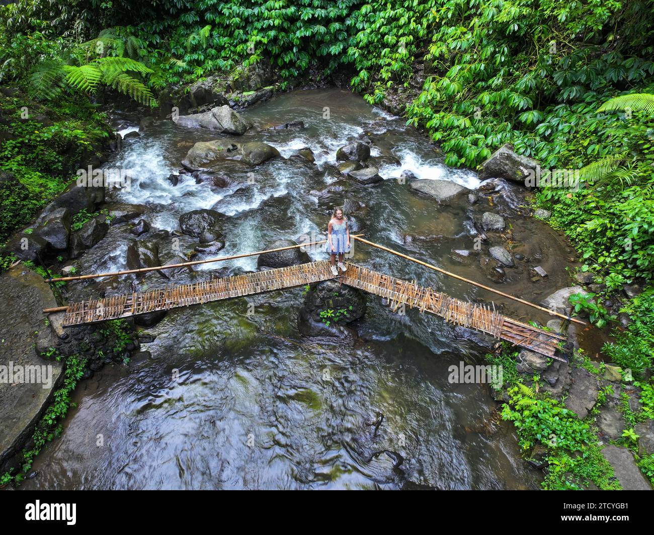 Ein junges Mädchen läuft auf einer kleinen Holzbrücke über den Dschungelbach, Bali Stockfoto