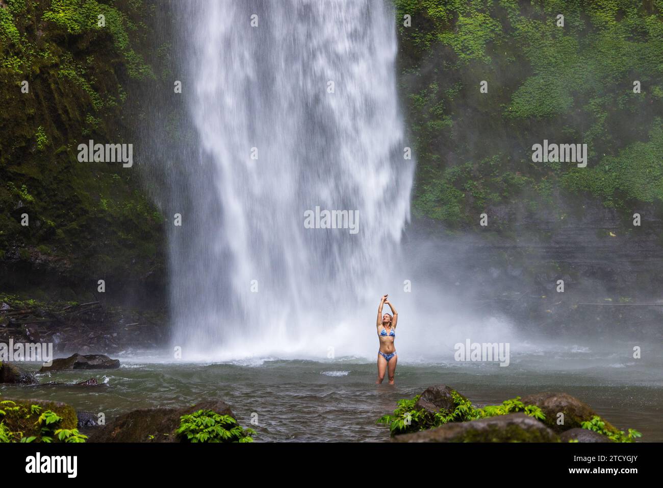 Eine junge Frau im Badeanzug am Nungnung Wasserfall im üppigen tropischen Wald, Bali, Indonesien Stockfoto