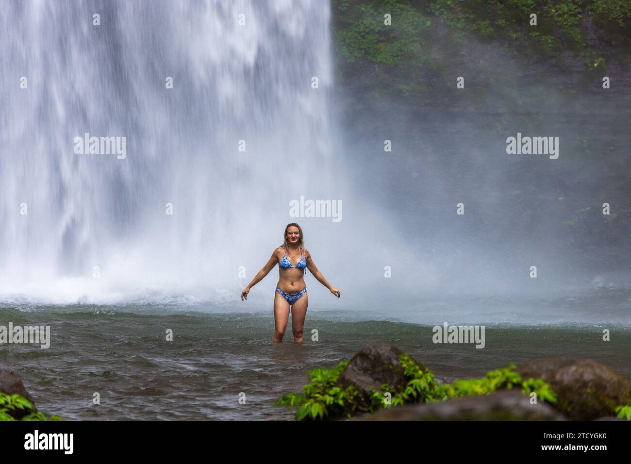 Eine junge Frau im Badeanzug am Nungnung Wasserfall im üppigen tropischen Wald, Bali, Indonesien Stockfoto