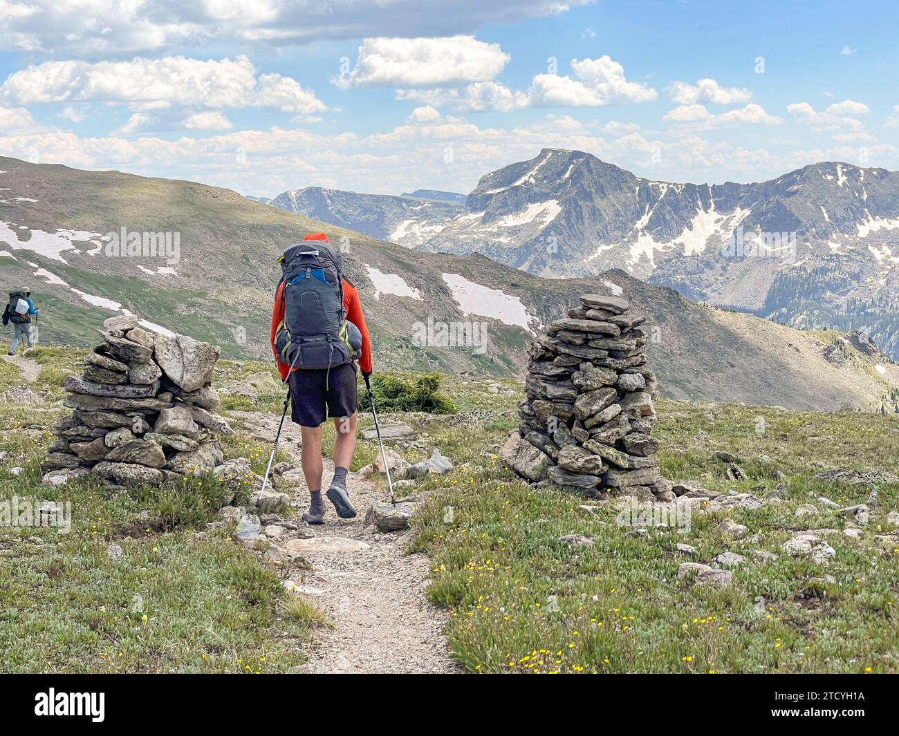 Ein männlicher Wanderer navigiert zwischen cairns auf dem North Inlet Trail, wobei sich die Pracht des Rocky Mountain National Park vor ihm erstreckt. Stockfoto