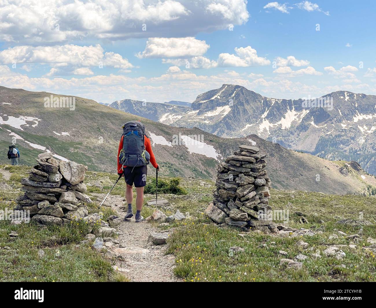 Ein männlicher Wanderer navigiert zwischen cairns auf dem North Inlet Trail, wobei sich die Pracht des Rocky Mountain National Park vor ihm erstreckt. Stockfoto