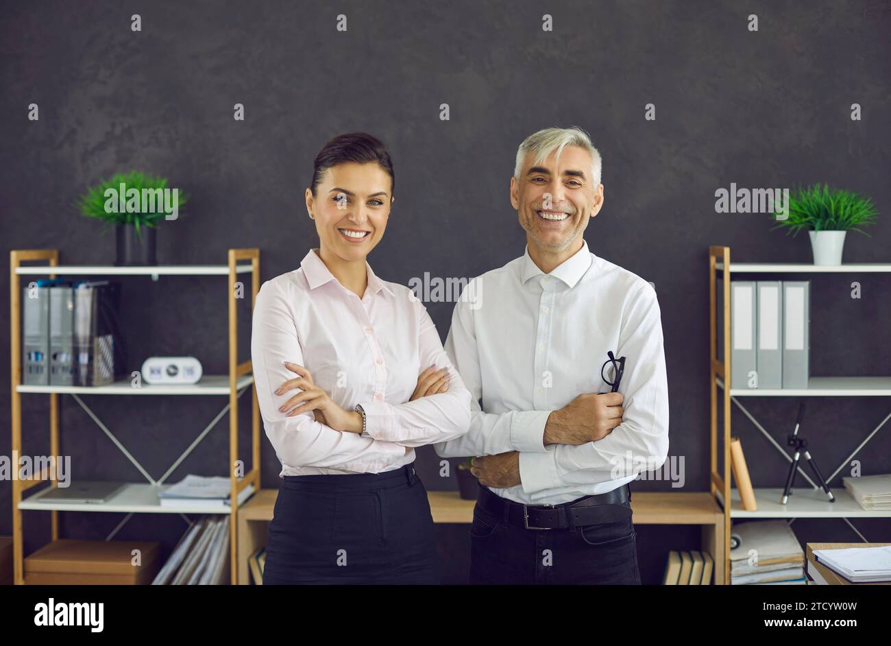 Glückliche junge Frau und ein älterer Mann stehen im Büro, schauen in die Kamera und lächeln Stockfoto