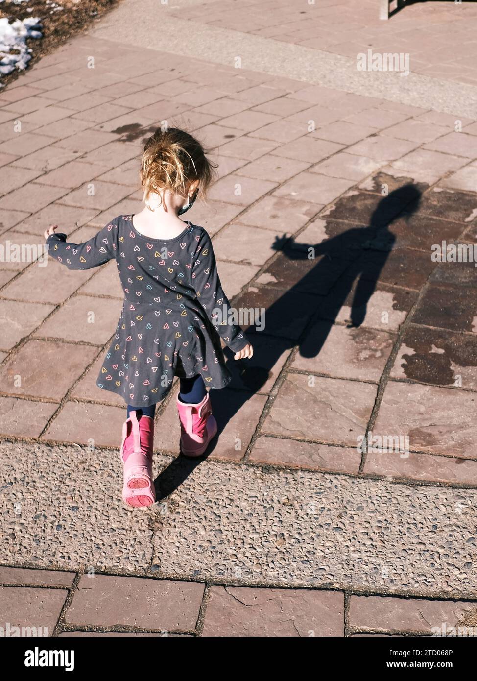 Kind in lässiger Kleidung, das im Frühling sonnig auf dem Fußweg spaziert Stockfoto