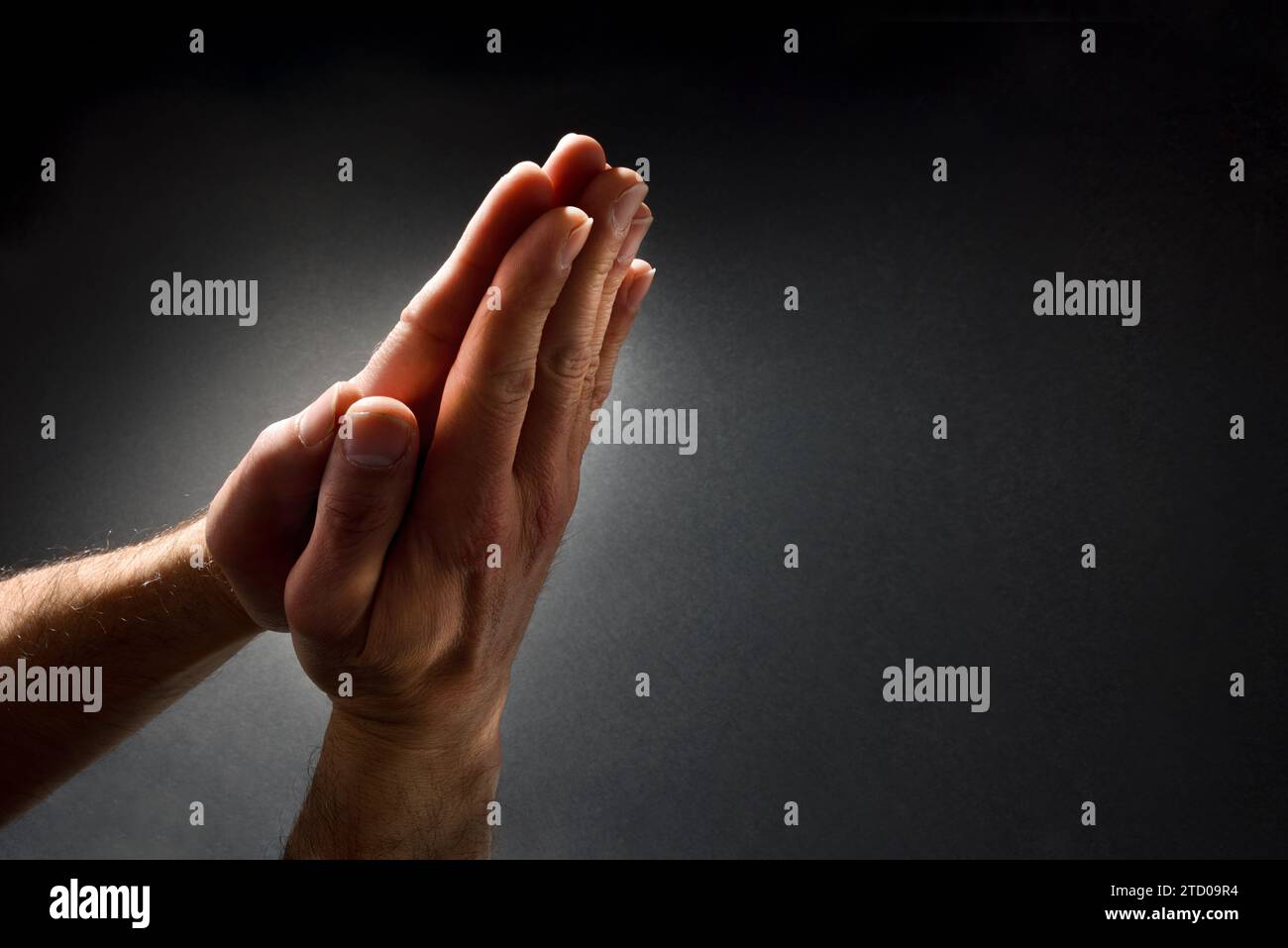 Betender Mann mit Händen mit Handflächen, kontrastiert mit Lichtstrahl auf dunklem, isoliertem Hintergrund. Erhöhte Ansicht von oben. Stockfoto