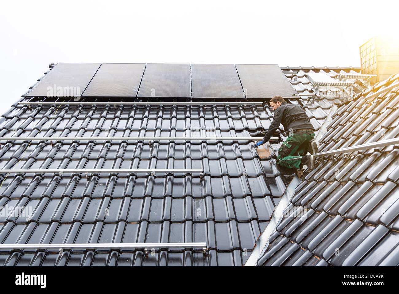 Ein Mann, der eine Sonnenkollektor-Anordnung auf dem Dach eines Hauses installiert Stockfoto