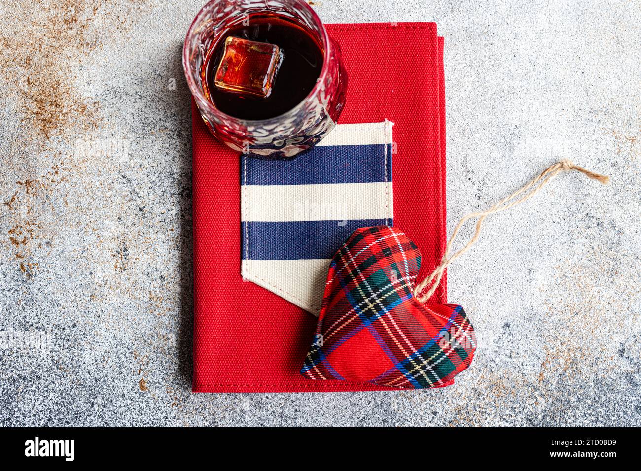 Ein rotes Hardcover-Buch mit einem karierten Stoffherz und einem Vintage-Glas auf der Oberseite, das die Liebe zur Vintage-Literatur repräsentiert. Stockfoto