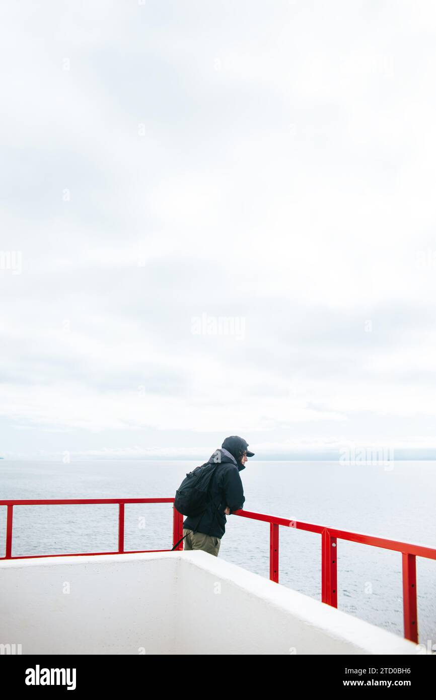 Ein Mann steht auf einem Fährdeck mit einem besinnlichen Blick über die ruhigen Gewässer von Vancouver Island, British Columbia, und genießt die Gelassenheit des Jou Stockfoto