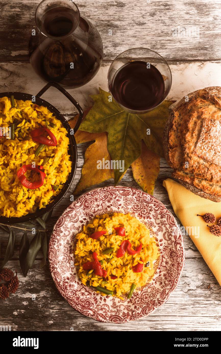 Ein rustikaler, herbstlicher Tisch mit Paella, handwerklichem Brot und einem Glas Rotwein, das warme, angenehme Speisen bietet, perfekt für die Saison. Stockfoto