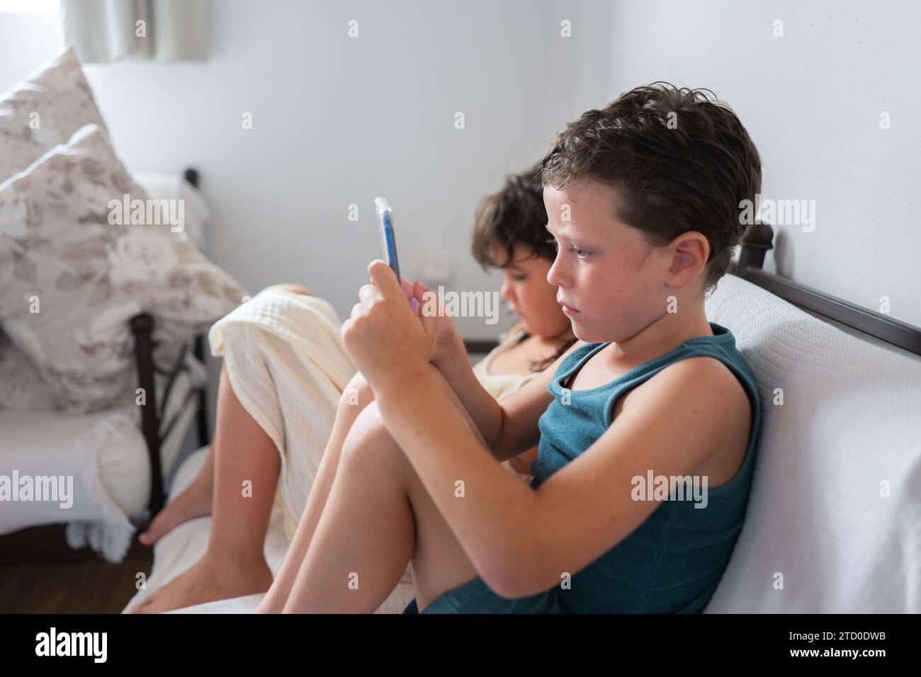 Seitenansicht von Schwester und Bruder in legeren Kleidern mit Mobiltelefon, während sie sich auf dem bequemen Sofa im Wohnzimmer entspannen Stockfoto