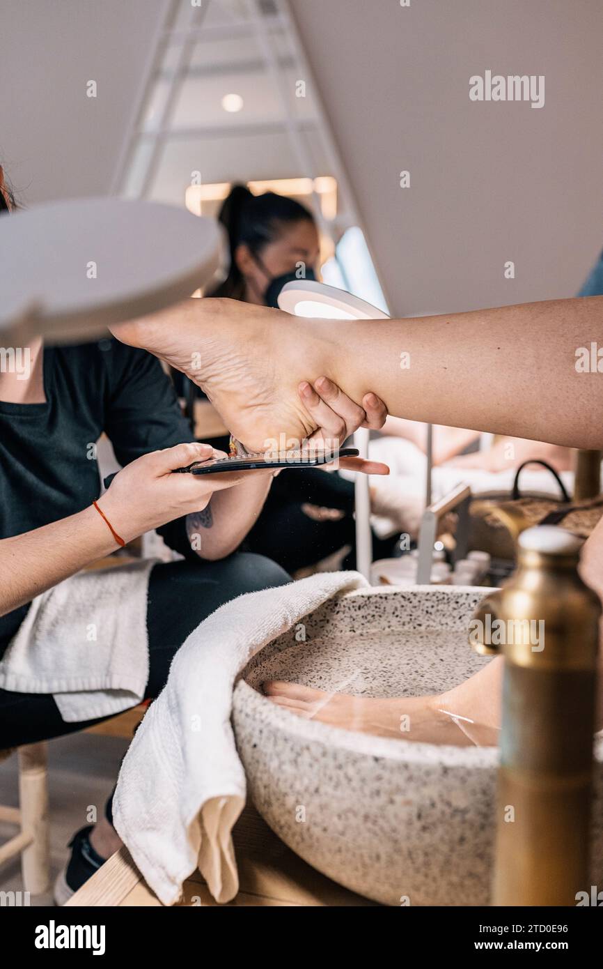 Beschneiden gesichtslose Hände des Masseurs, der Pediküre mit Pinsel und Wasserfüße in einem modernen Schönheitssalon macht Stockfoto