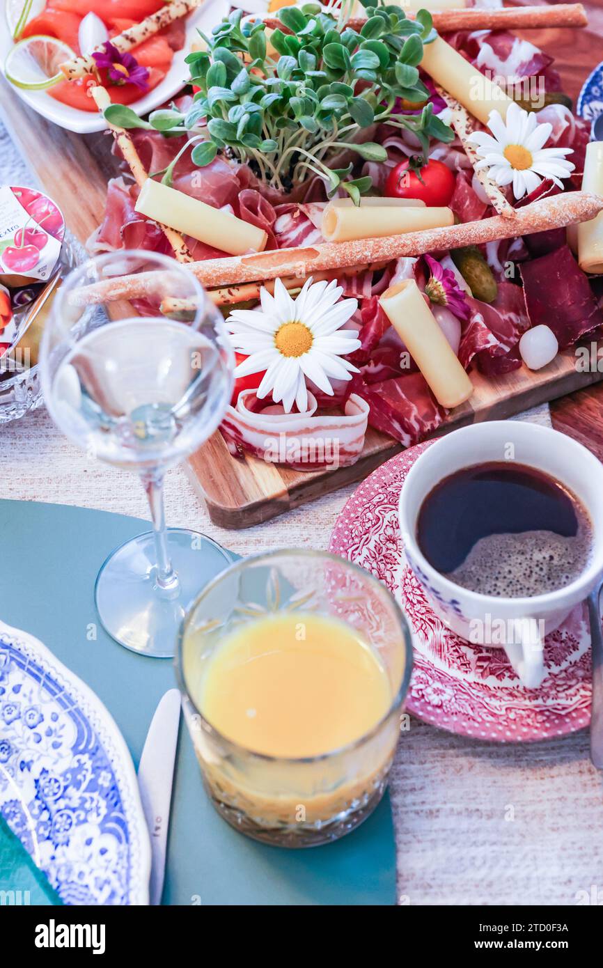 Eine stilvolle Wurstplatte gefüllt mit verschiedenen Aufschnitten, Käse und frischen Beilagen, begleitet von Wein, frischem Saft, und Kaffee. Stockfoto