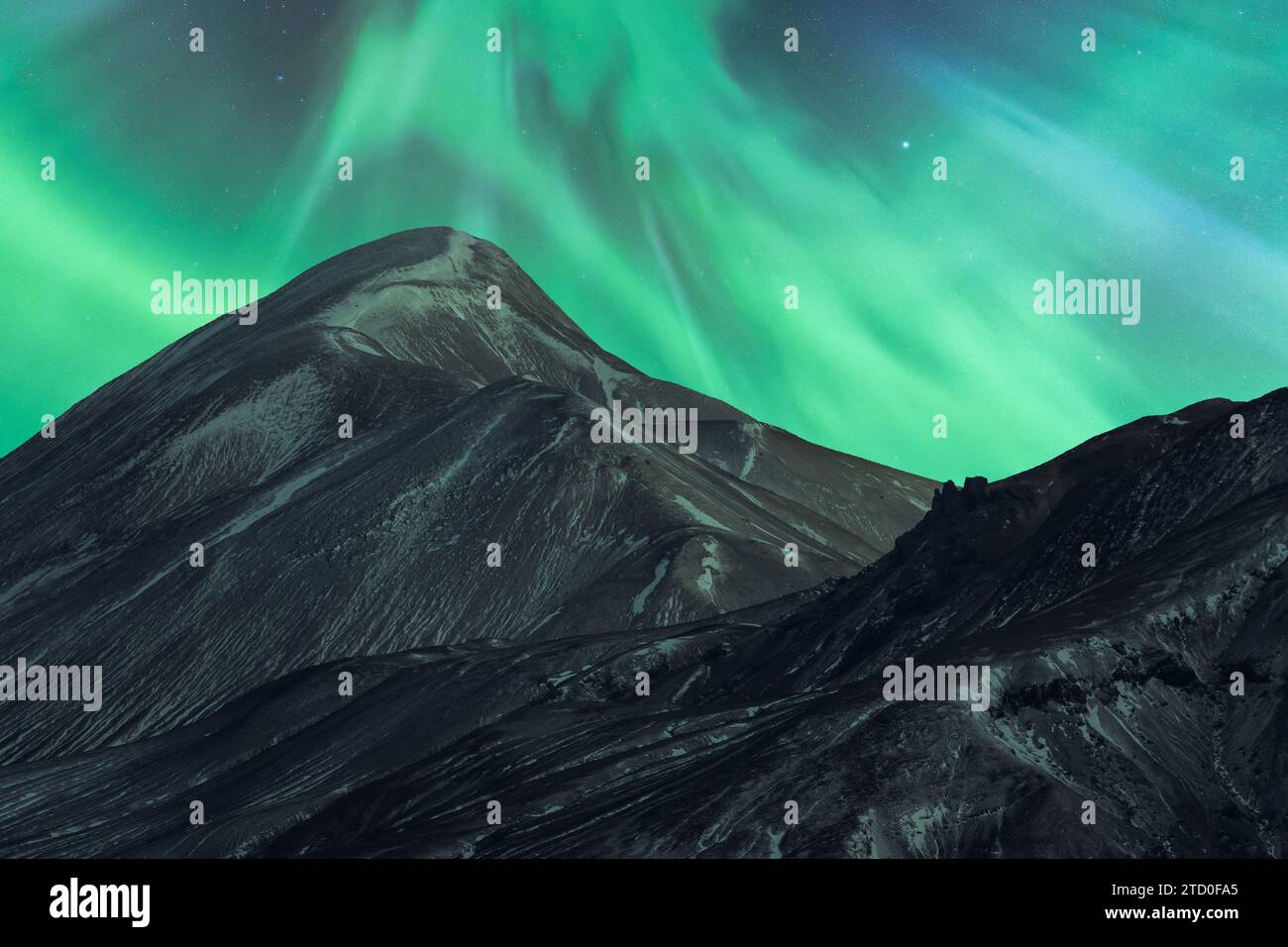 Faszinierende Nordlichter tanzen über einem dunklen, zerklüfteten Berggipfel in der isländischen Wildnis und zeigen die natürliche Schönheit. Stockfoto