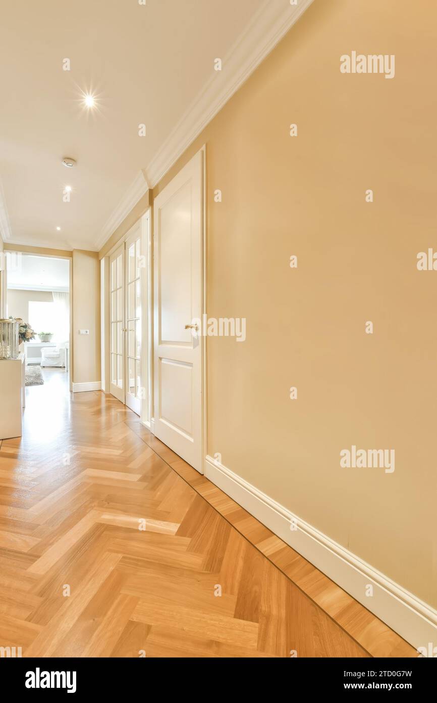 Leerer langer Flur mit beigefarbenen Wänden und weißen Türen führt zu verschiedenen Zimmern in einem modernen Apartment Stockfoto