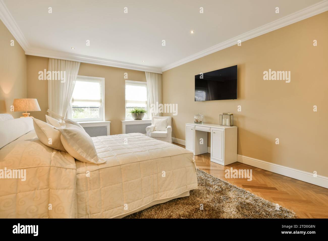 Innenraum des Schlafzimmers mit gemütlichem weißem Bett vor dem Fernseher, der an der beigefarbenen Wand in einem modernen Apartment montiert ist Stockfoto