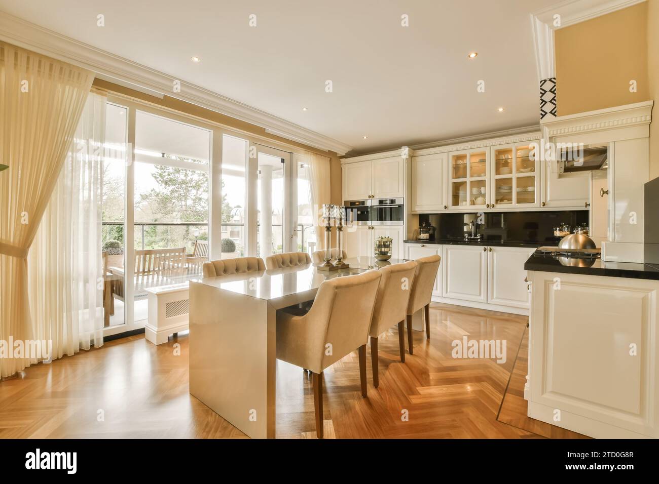 Esstisch und Stühle sind vor einer offenen, großen Küche neben einem hellen Fenster in einem modernen Apartment angeordnet Stockfoto