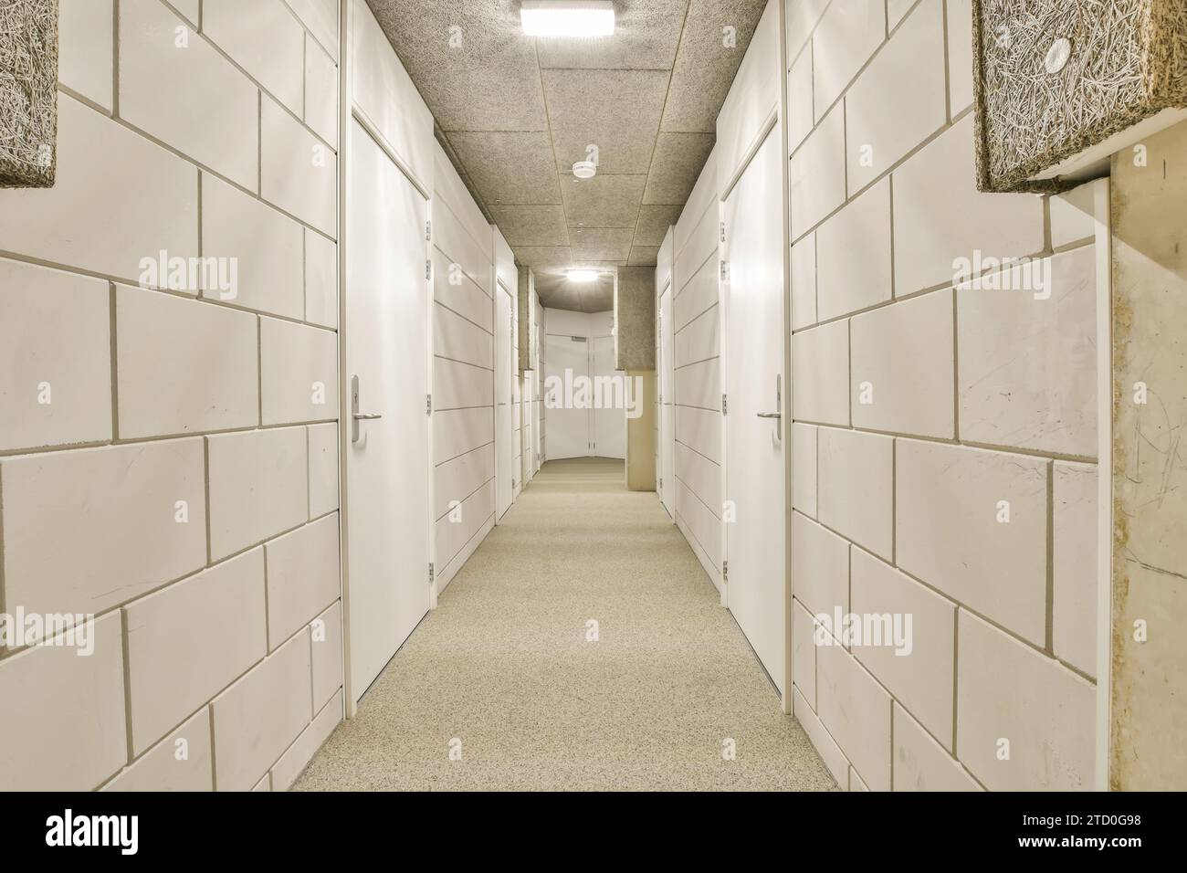 Langer schmaler Korridor mit weißen Fliesenwänden und geschlossenen Türen von Lagerräumen im Industriegebäude zur Vermietung Stockfoto