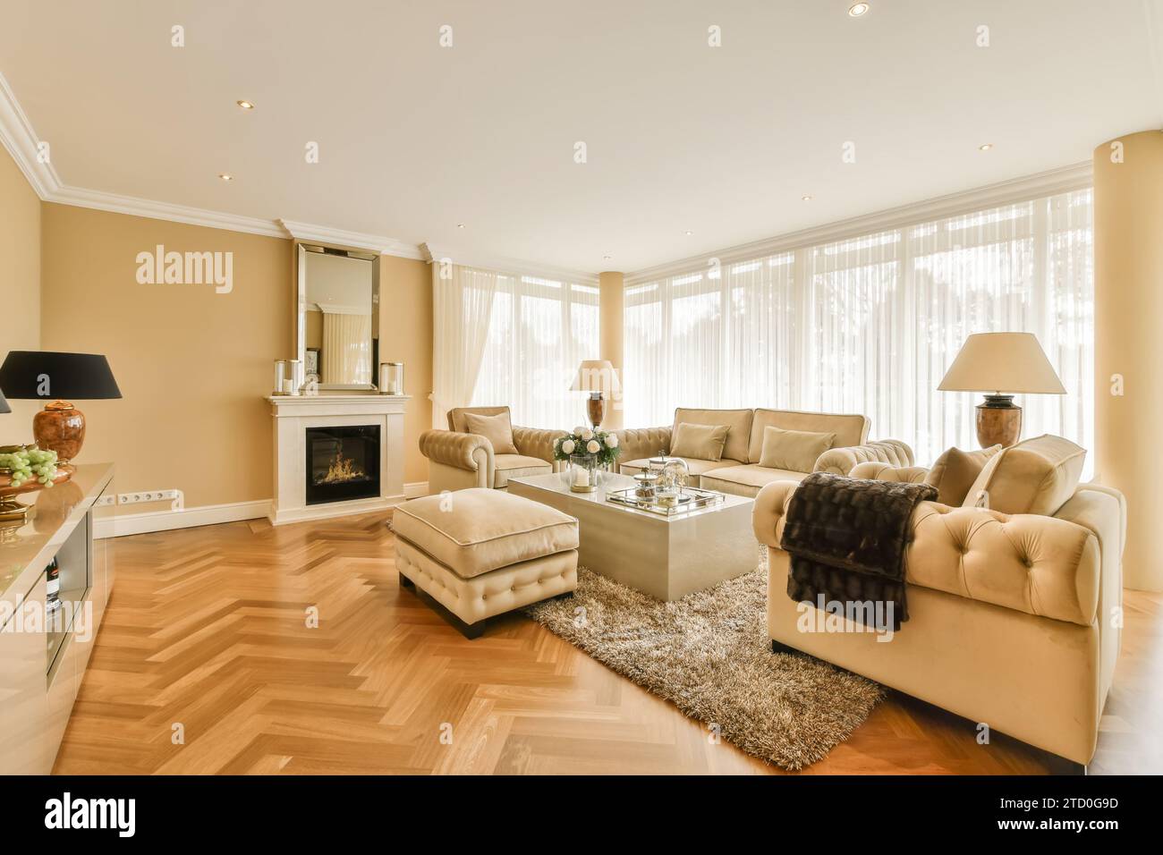 Sofa mit Sesseln und Couchtisch durch Fenster vor dem Kamin im geräumigen, modernen Wohnzimmer Stockfoto