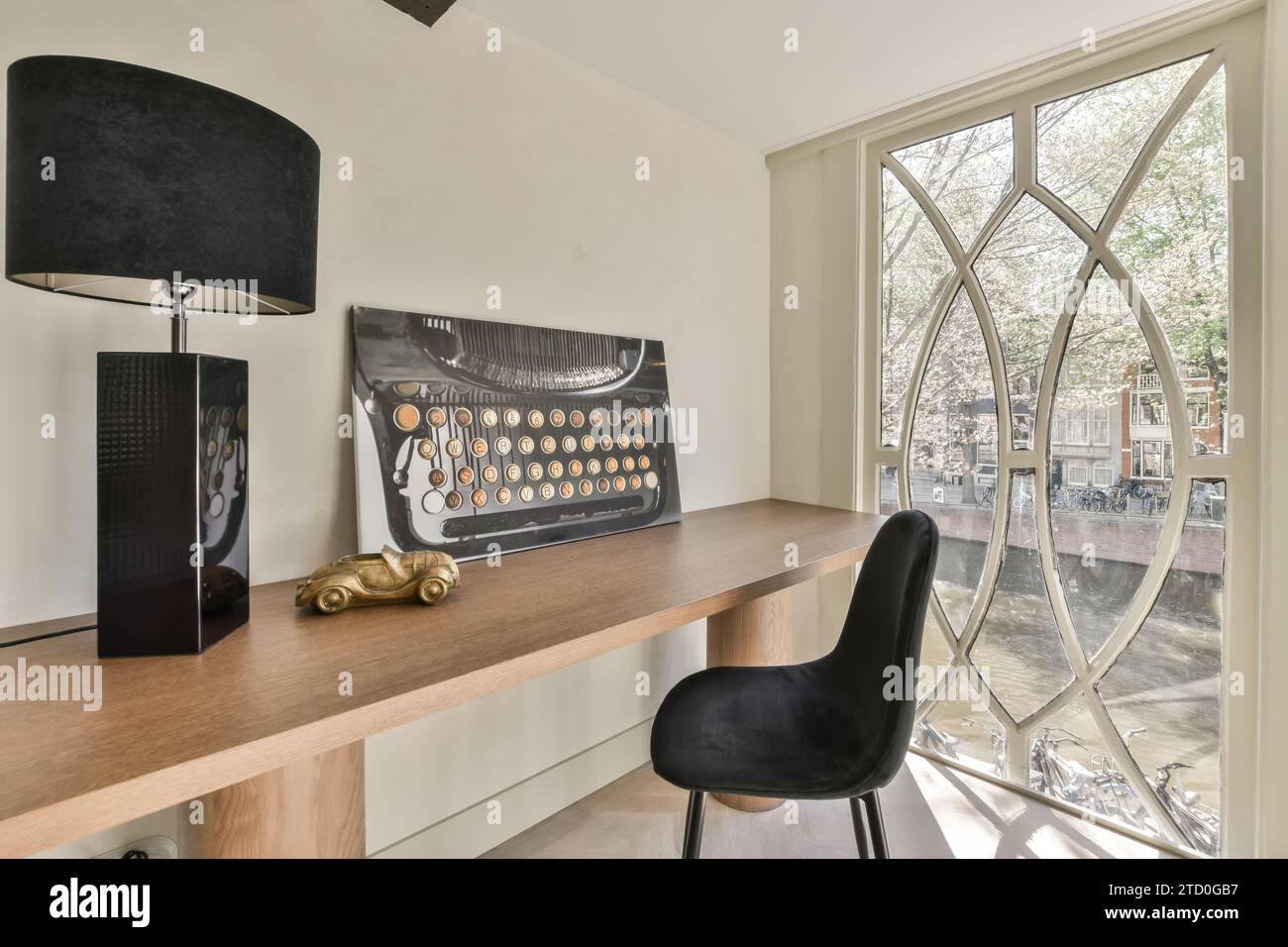 Antiquitäten mit Lampe auf Holzschreibtisch mit schwarzem Stuhl neben Fenster in zeitgenössischem Apartment Stockfoto