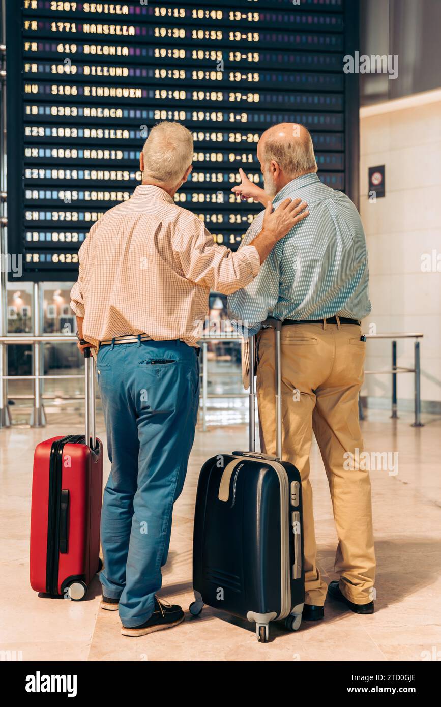 Rückansicht von anonymen älteren männlichen Touristen in ungezwungener Kleidung, die auf der Abflugplantafel am zeitgenössischen Flughafen während des Urlaubs schauen Stockfoto