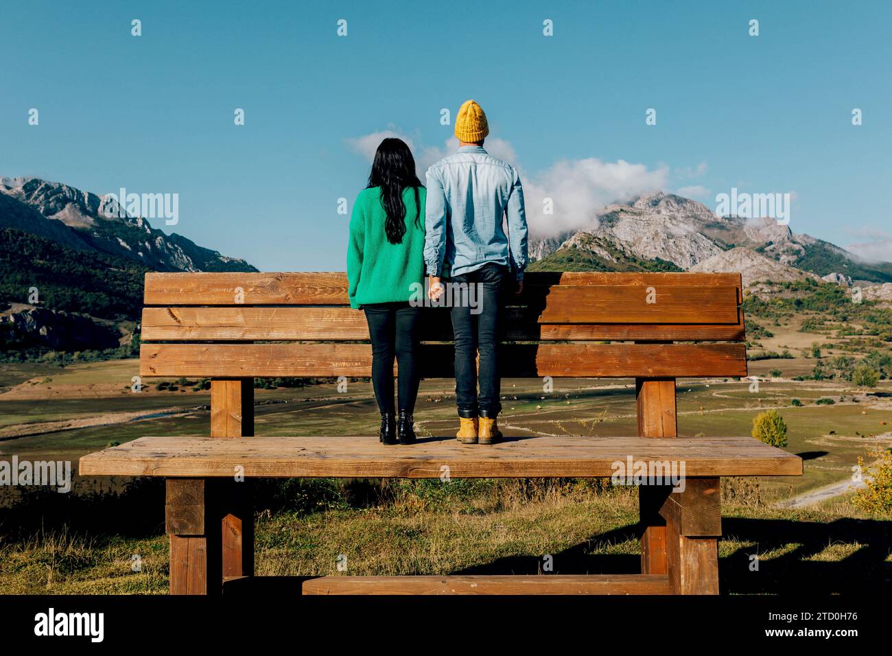 Eine Rückansicht eines Paares in legerer Kleidung, das Hände hält und den malerischen Blick auf die Berge betrachtet. Stockfoto