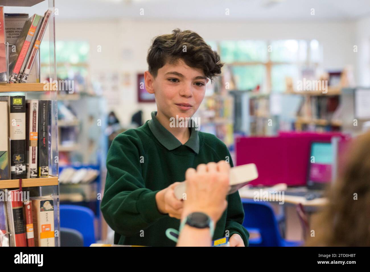 Ein männlicher Schüler checkt ein Buch in der Schulbibliothek mit dem Bibliothekar Stockfoto