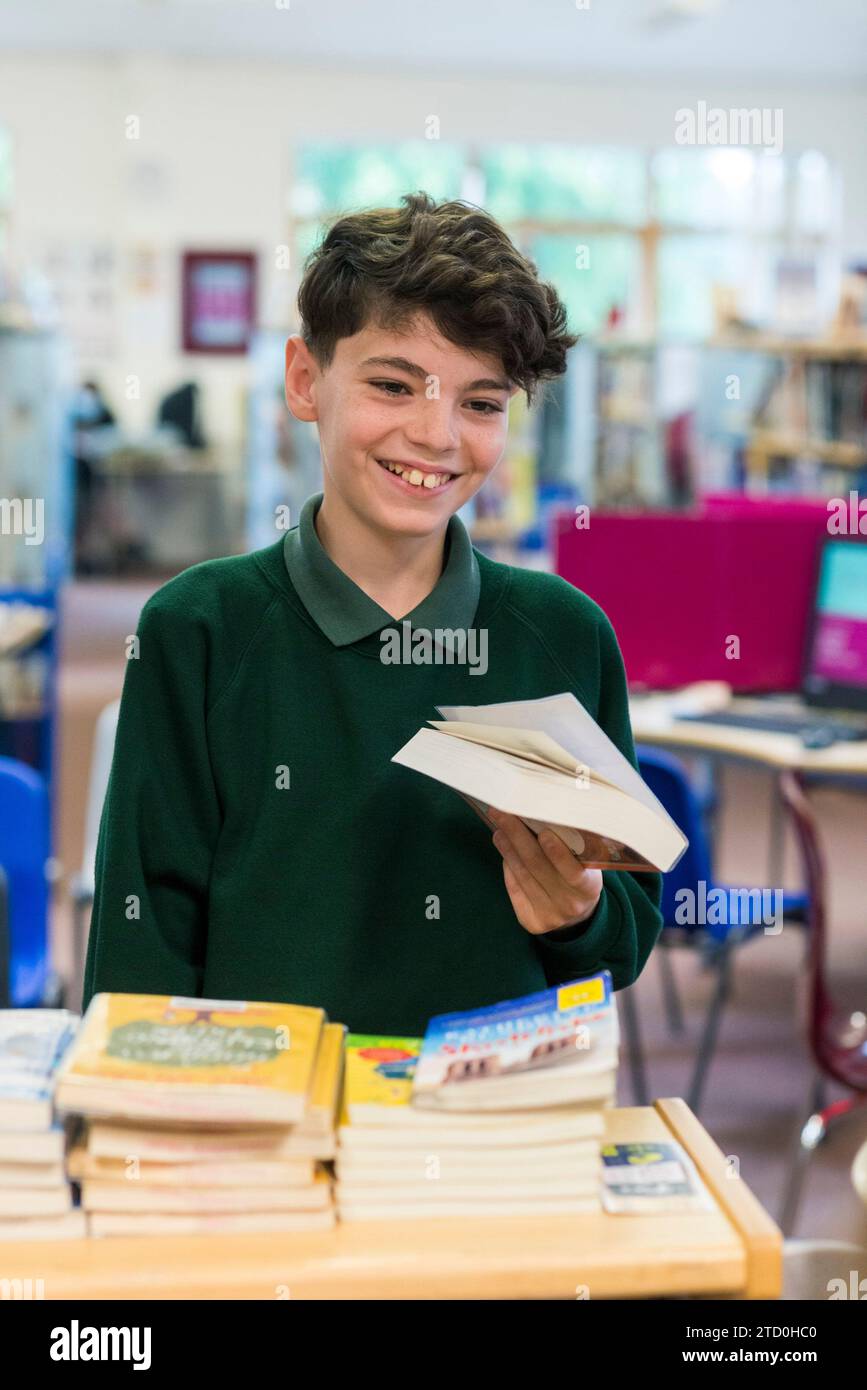 Ein männlicher Schüler checkt ein Buch in der Schulbibliothek mit dem Bibliothekar Stockfoto