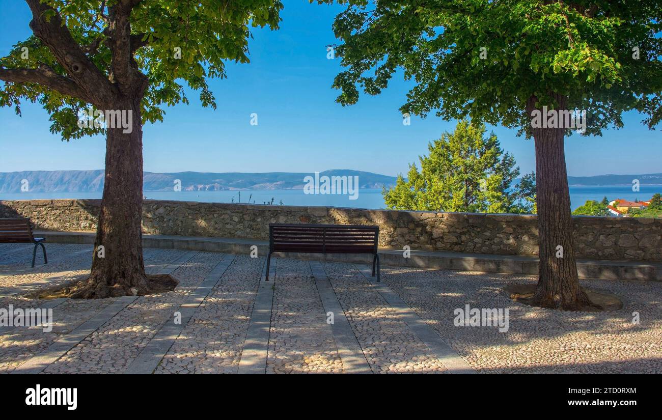 Eine Bank mit Blick auf das Meer im Stari Grad historischen Zentrum von Novi Vinodolski, Komitat Primorje-Gorski Kotar, Kroatien. Krk Island im Hintergrund Stockfoto