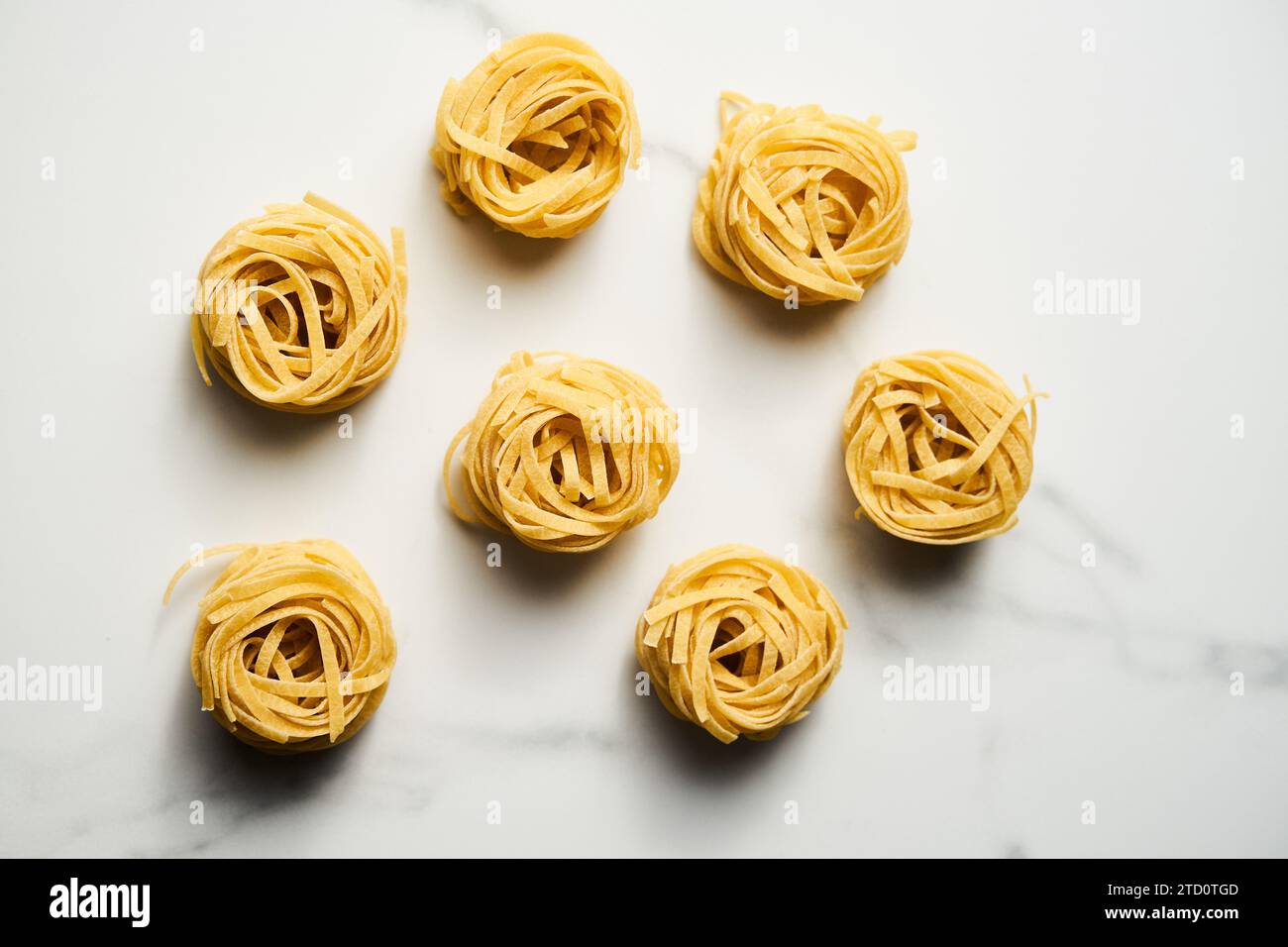 Trockene Tagliolini- oder Tagliatelle-Pasta in Nestern in der Schüssel auf weißem Marmorhintergrund. Ungekochte Zutat Stockfoto