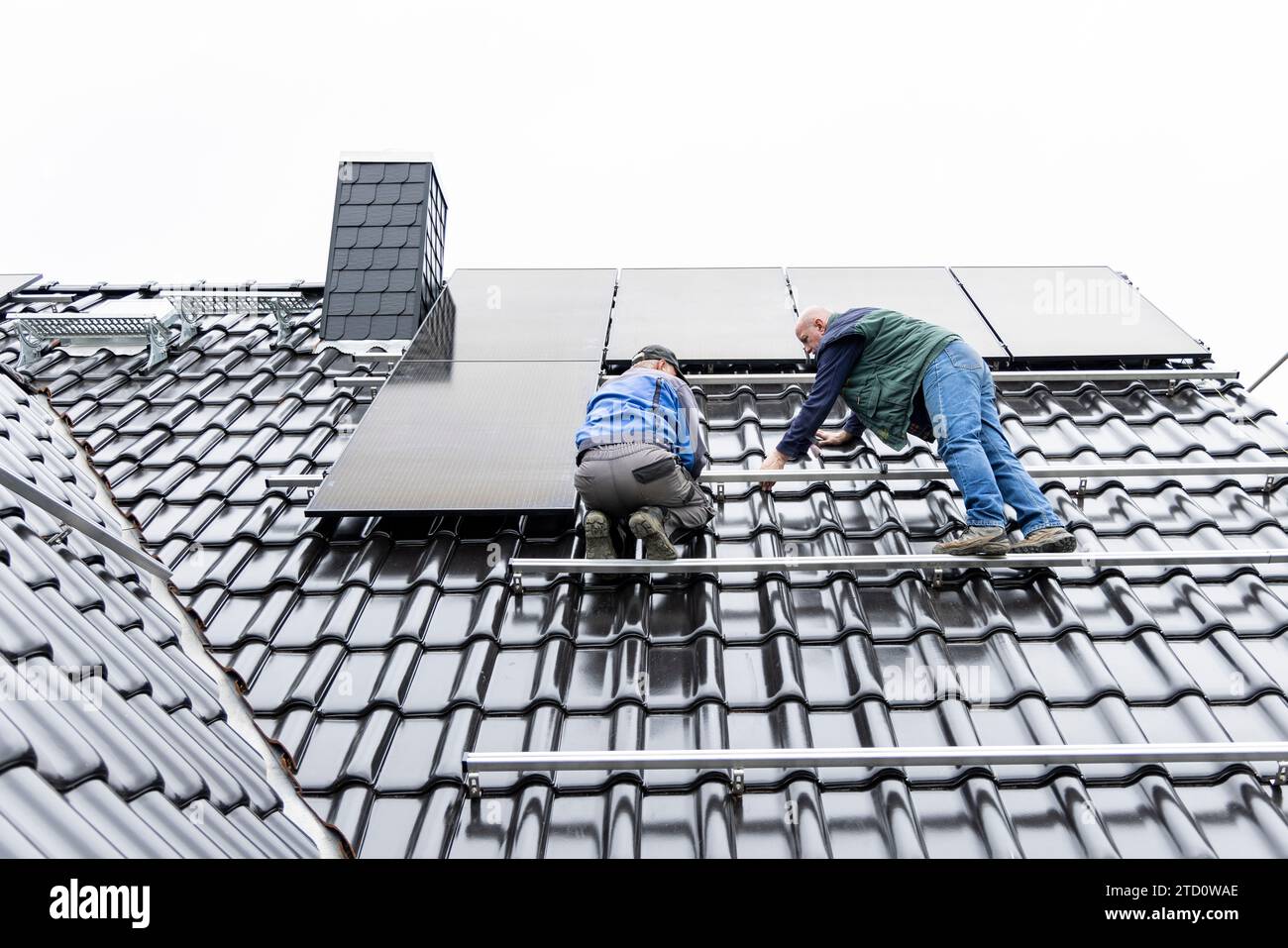 Zwei Techniker, die an der Installation einer Photovoltaikanlage auf dem Dach eines Hauses arbeiten Stockfoto