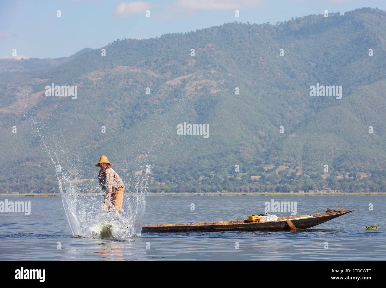 Ein traditioneller einbeiniger Intha-Burmese-Fischer auf seinem Holzboot mit den Bergen im Hintergrund, Inle Lake, Shan State, Myanmar. Stockfoto