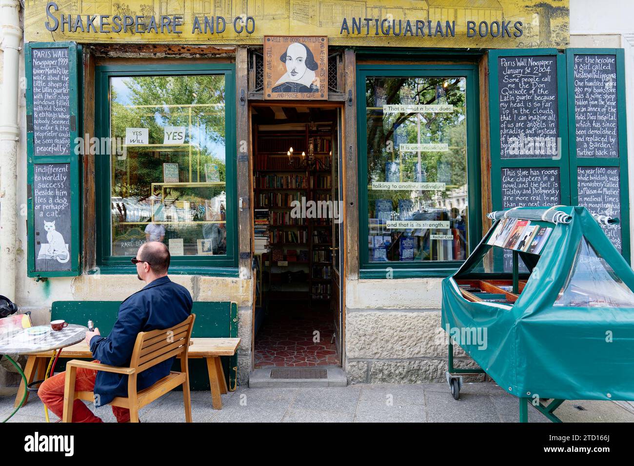 Eine Person sitzt neben einem der Eingänge des Buchladens Shakespeare and Company. Antiquarische Bücher. Pariser Literatursymbol. Stockfoto