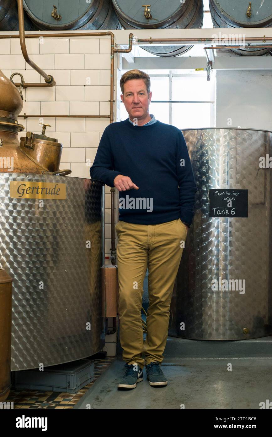 Ein männlicher Kleinunternehmer steht mit seiner Gin-Ausrüstung in einer handwerklichen Destillerie. Stockfoto