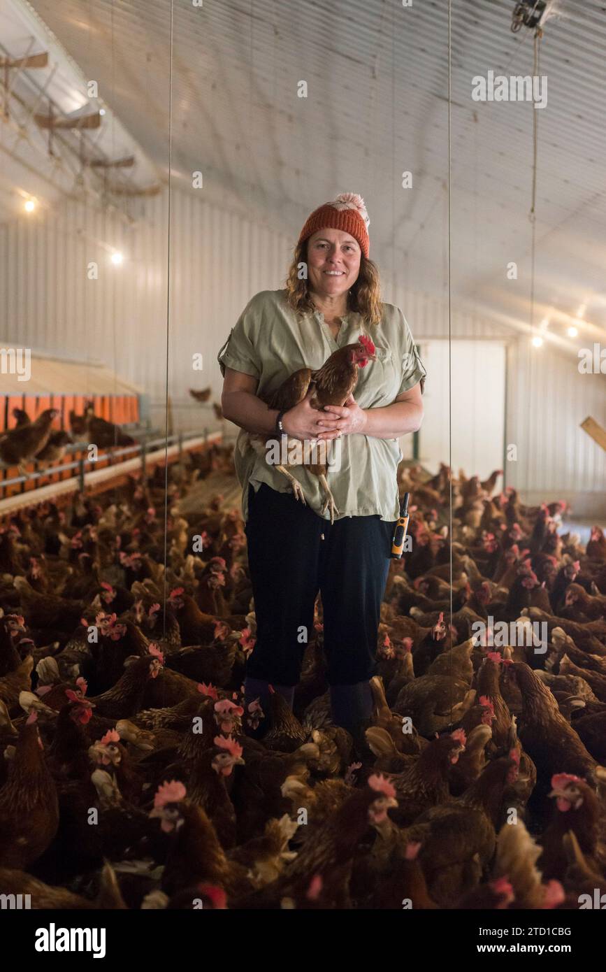 Eine Farmerin hält ein Huhn, umgeben von Hühnern und Hühnern. Stockfoto