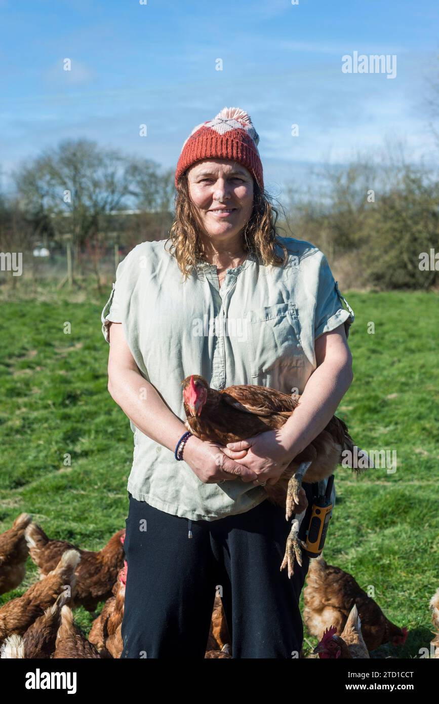 Eine Farmerin hält ein Huhn, umgeben von Hühnern und Hühnern. Stockfoto