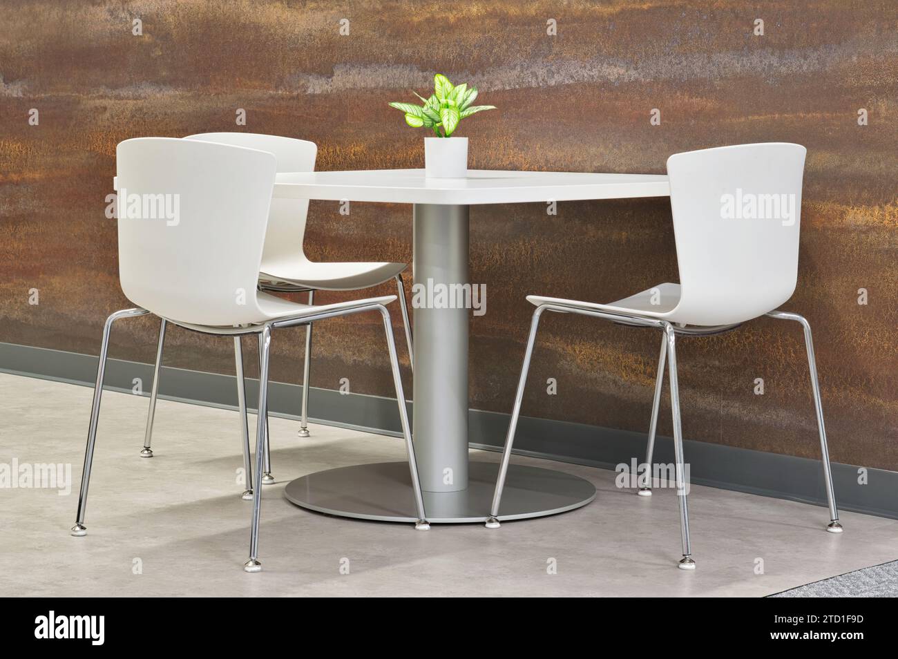 Moderne Inneneinrichtung, weißer Tisch und Stuhl mit künstlicher Pflanze neben der Wand. Küche und Pausenraum Möbel. Stockfoto