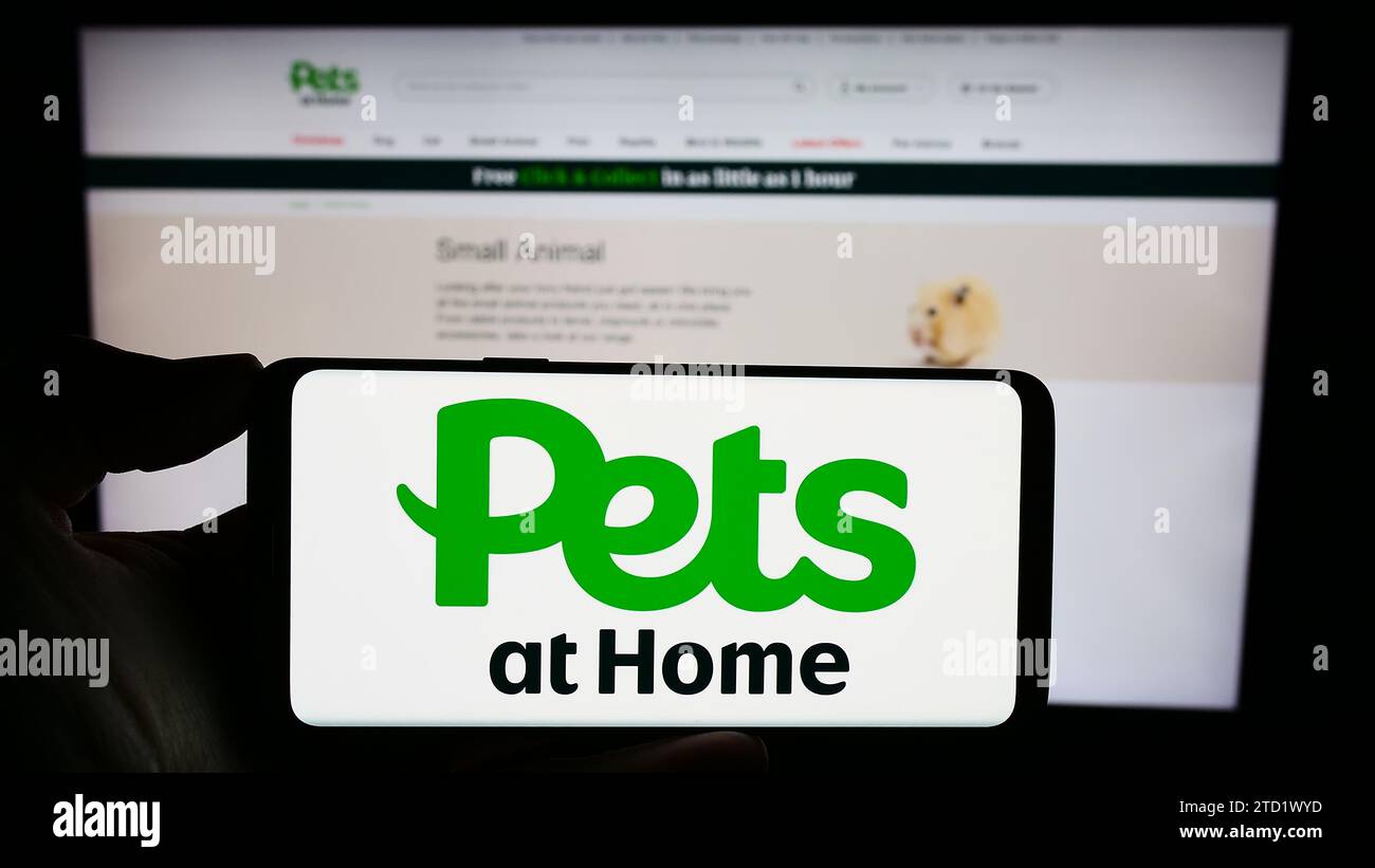 Person, die ein Mobiltelefon mit dem Logo des britischen Einzelhandelsunternehmens Pets at Home Group vor der Website des Unternehmens hält. Schwerpunkt auf dem Display des Telefons. Stockfoto