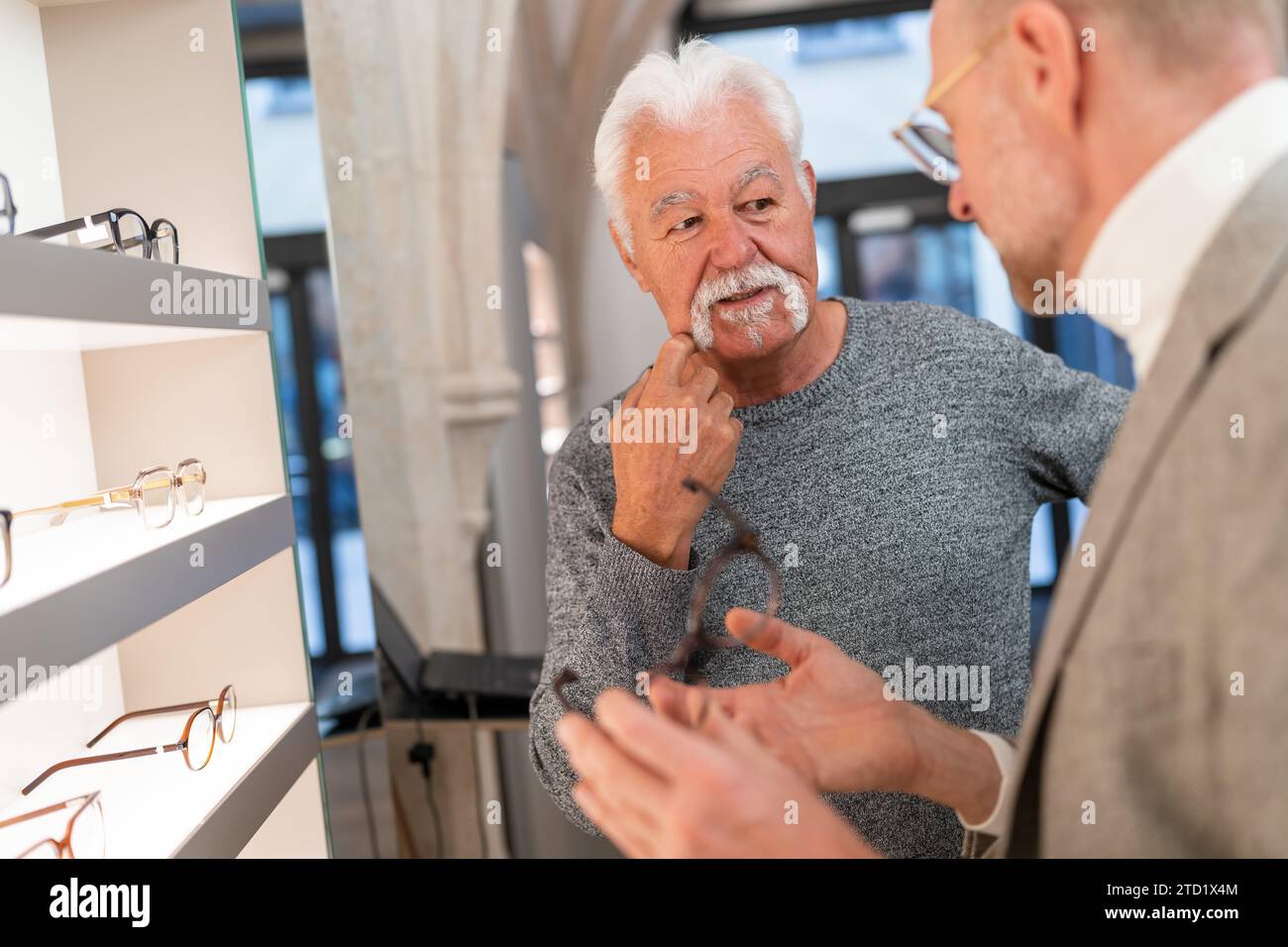 Älterer Mann, der mit Optiker im Optikgeschäft über eine Brille nachdenkt Stockfoto