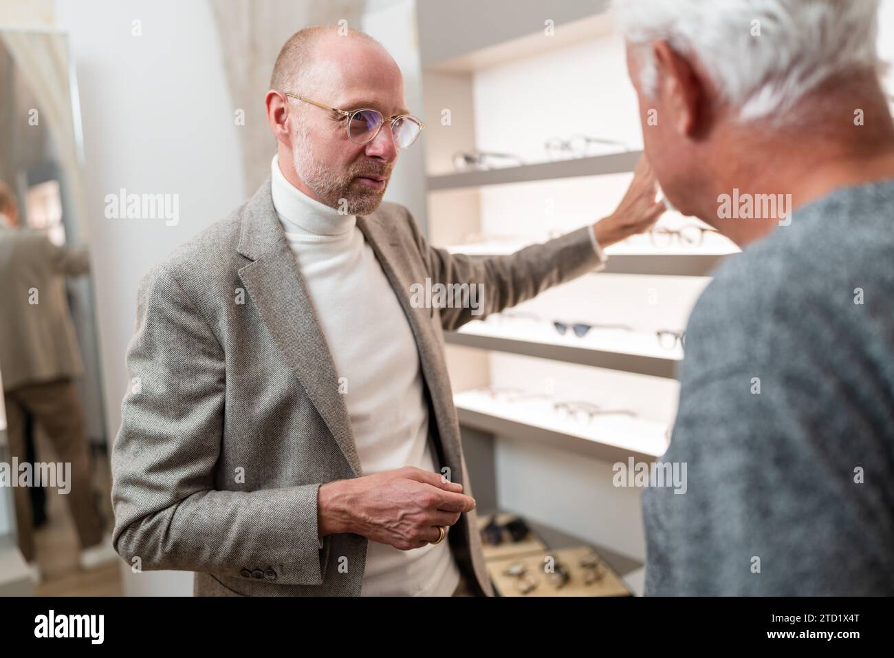 Augenoptiker zeigt älteren Kunden Brillen im optischen Geschäft und erklärt verschiedene Brillenmodelle. Stockfoto