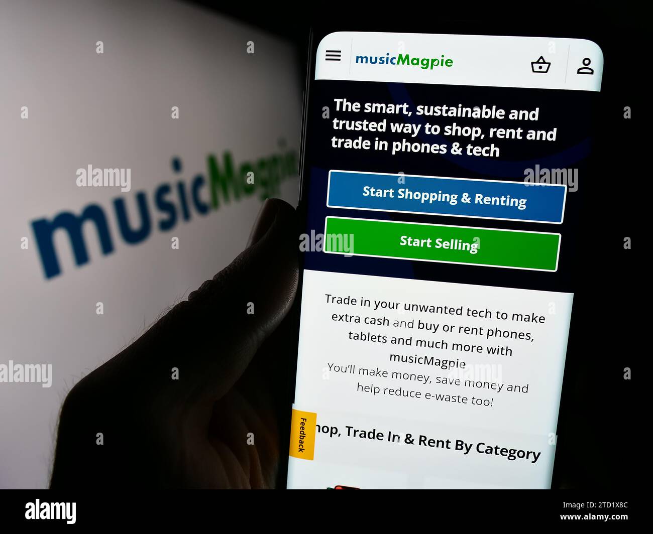 Person mit Smartphone und Webseite des britischen E-Commerce-Unternehmens MusicMagpie vor dem Firmenlogo. Konzentrieren Sie sich auf die Mitte des Telefondisplays. Stockfoto