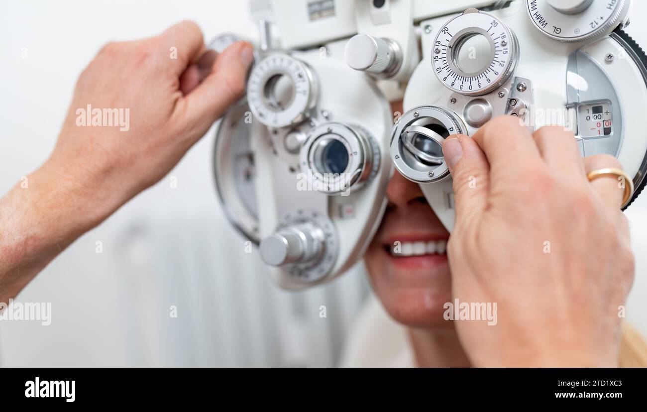 Nahaufnahme eines Optikers, der einen Phoropter für eine Patientin während eines Augentests an der Augenklinik justiert. Gesundheitswesen und Medizinkonzept Stockfoto