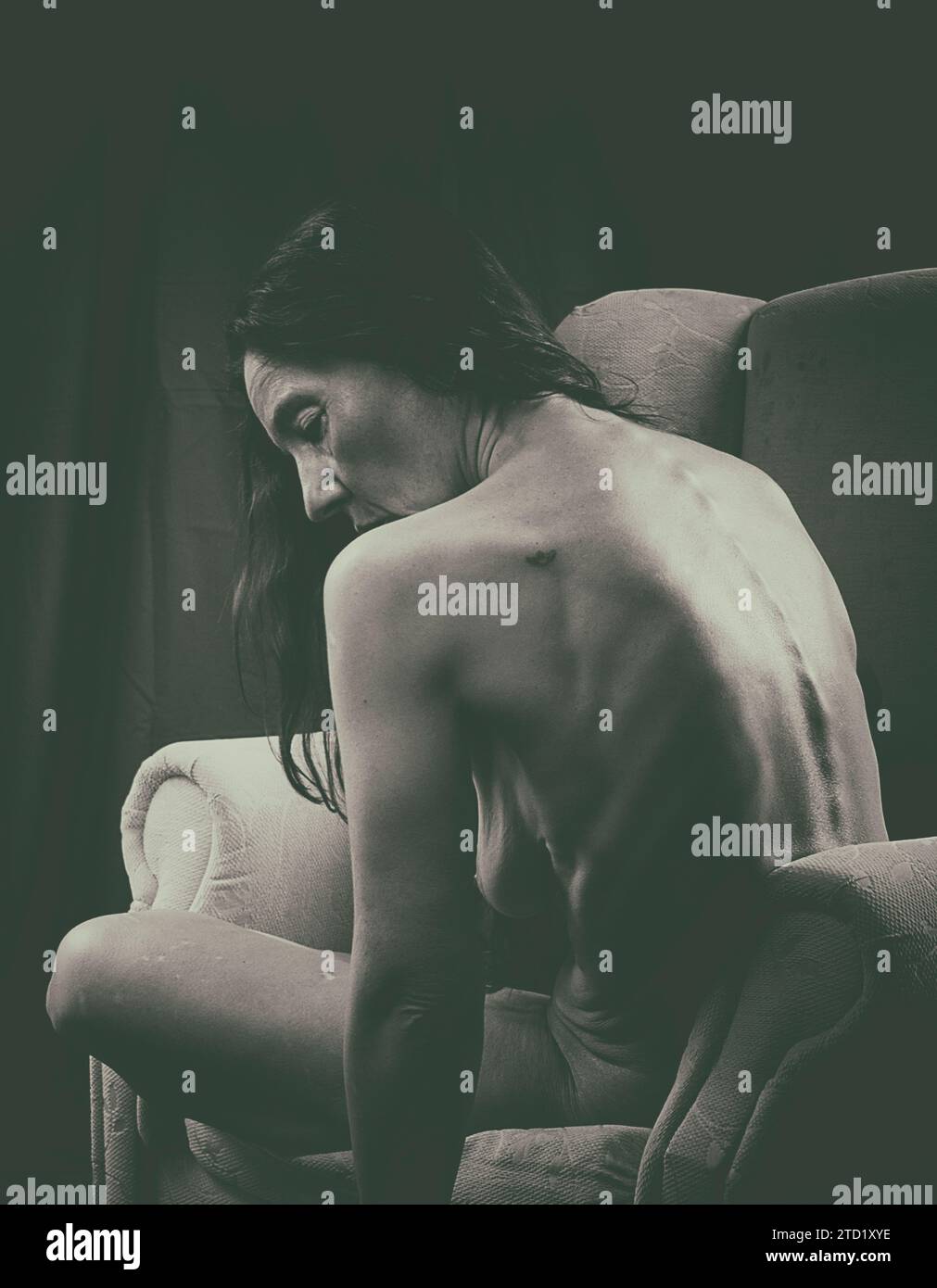 Frau sitzt und zeigt ihren nackten Rücken in einem Sessel III Stockfoto