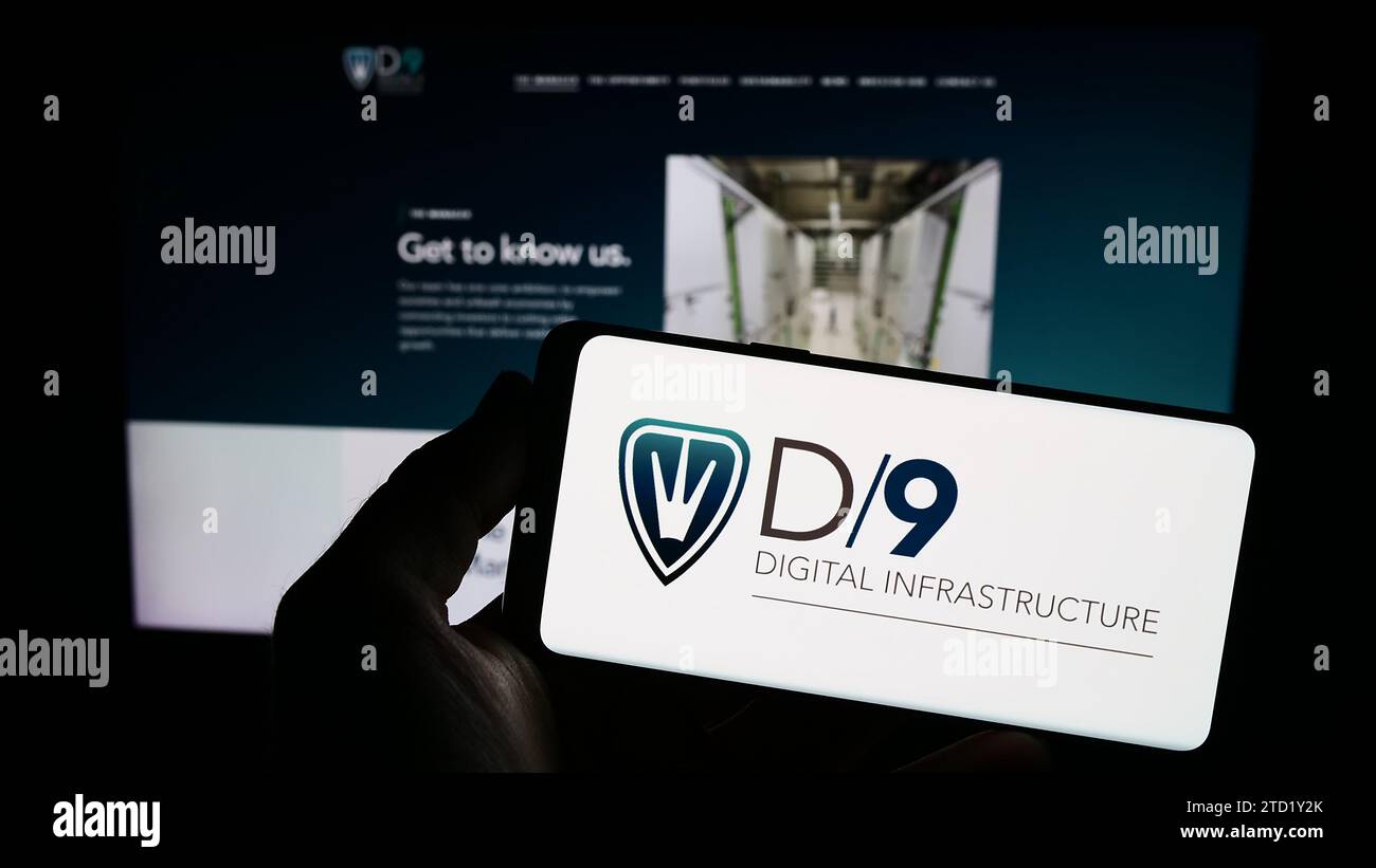 Person mit Smartphone und Logo des britischen Unternehmens Digital 9 Infrastructure plc (D9) vor der Website. Schwerpunkt auf dem Display des Telefons. Stockfoto