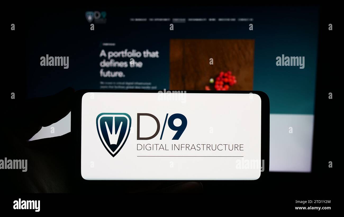 Person, die ein Mobiltelefon mit dem Logo des britischen Unternehmens Digital 9 Infrastructure plc (D9) vor der Unternehmenswebseite hält. Schwerpunkt auf dem Display des Telefons. Stockfoto